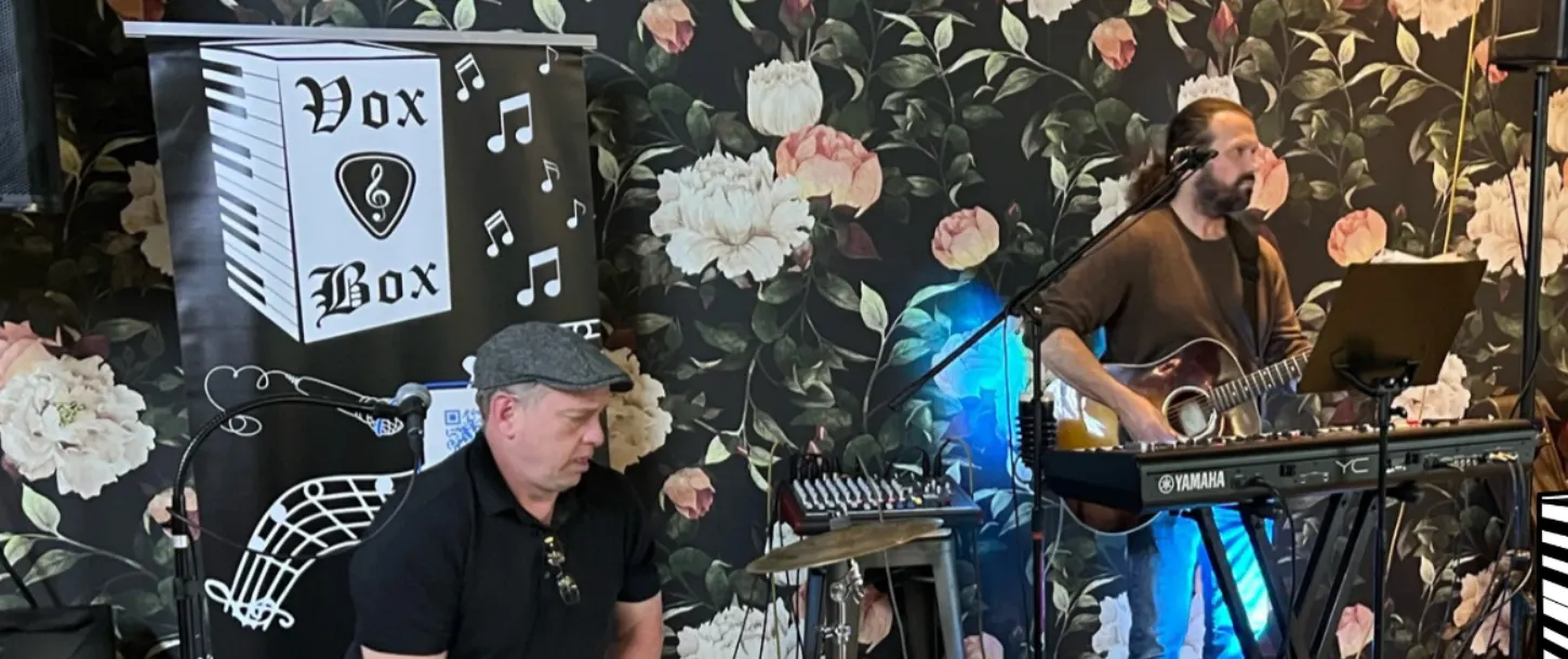 Vox & Box Duo on stage with guitar, keys, and percussion